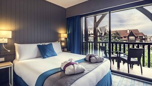 A hotel room with a large bed, two bedside lamps, a view of the balcony, and a cityscape in the background. - Mercure Deauville Centre (Deauville)