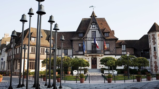 A historic building with a prominent clock tower, surrounded by a courtyard with potted plants and a series of street lamps. - Mercure Deauville Centre (Deauville)