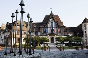 A historic building with a prominent clock tower, surrounded by a courtyard with potted plants and a series of street lamps. - Mercure Deauville Centre (Deauville)