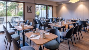 A modern dining area with tables and chairs, large windows, and pendant lighting. - Mercure Deauville Centre (Deauville)
