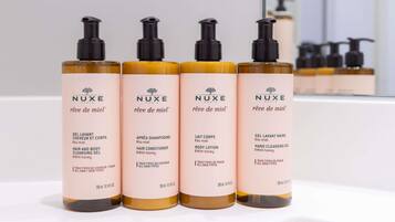 Cuatro botellas de productos para el cabello y el cuerpo de Nuxe Paris sobre una superficie blanca.