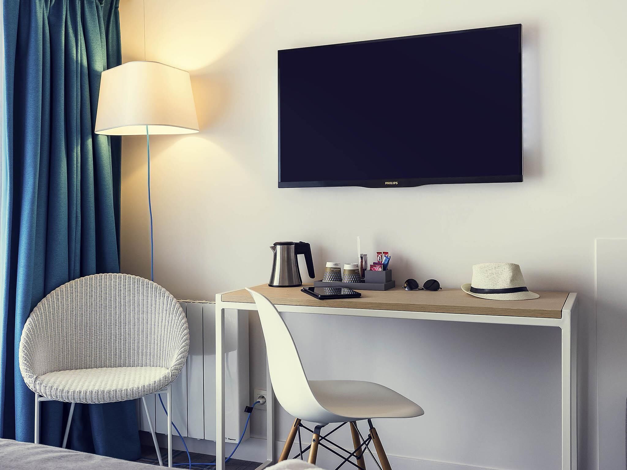 A hotel room with a desk, chair, television, and a lamp.