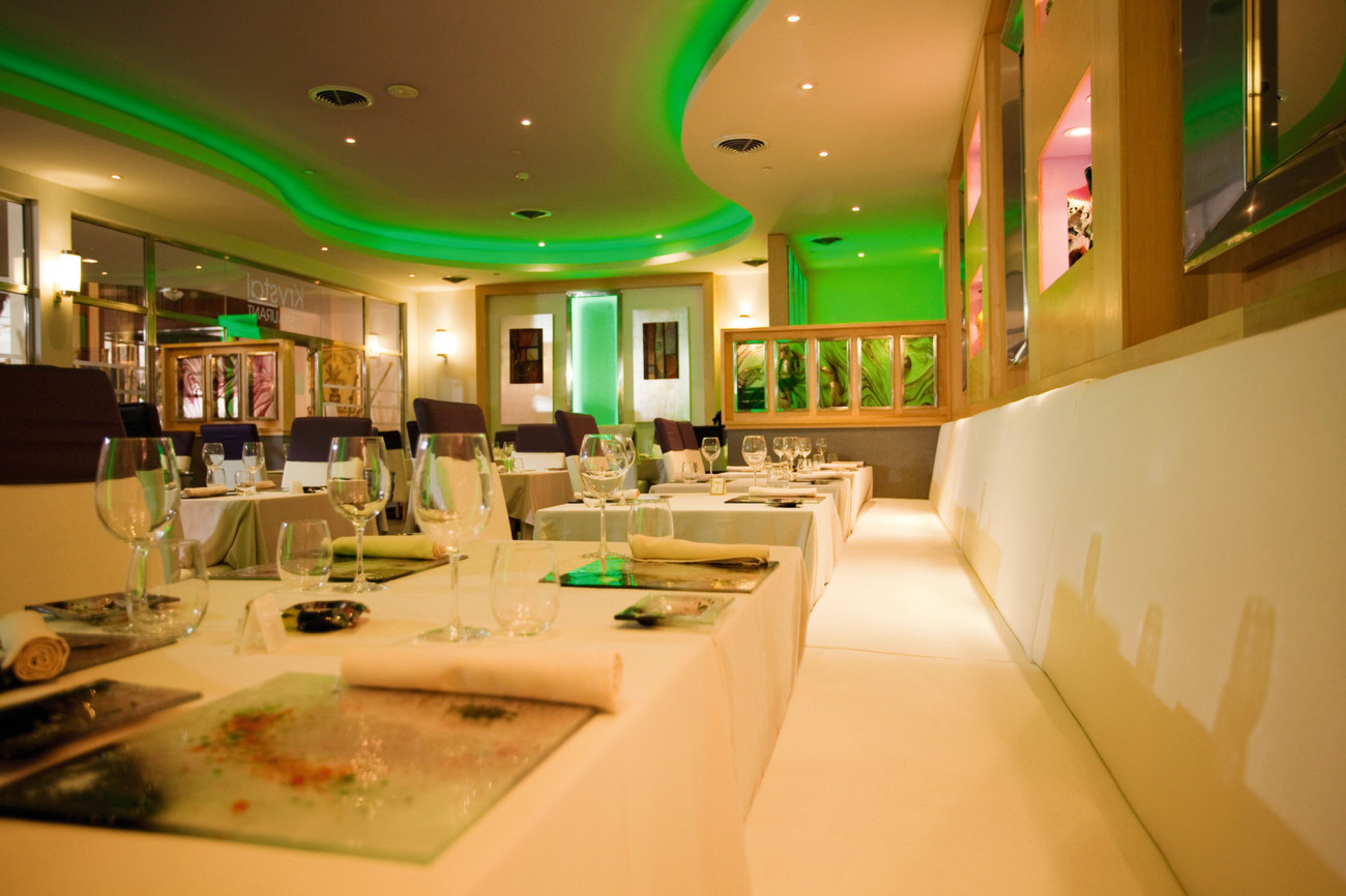 A restaurant with multiple tables set for dining, featuring a modern interior design with green ambient lighting.