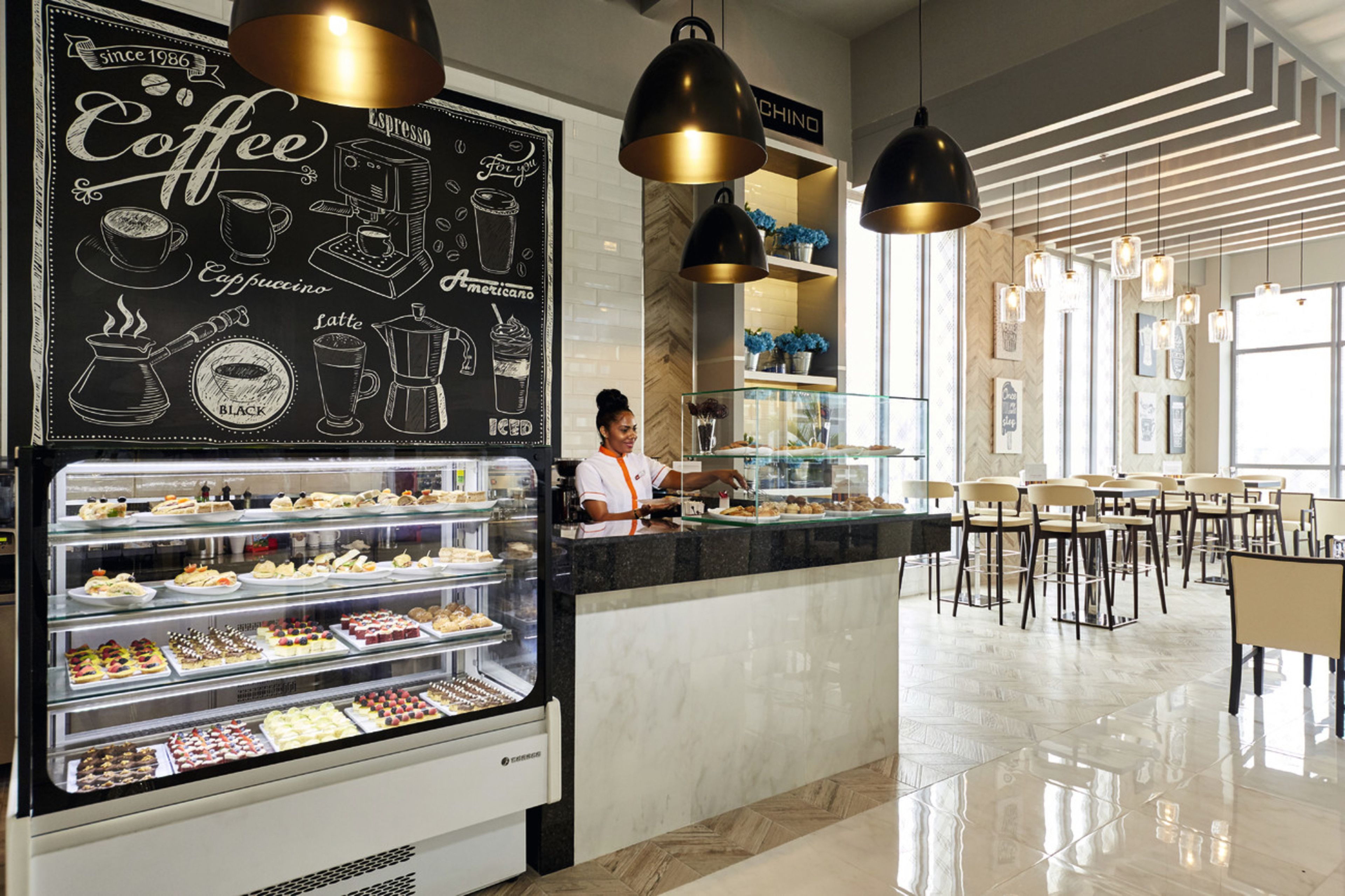 Een modern koffiehuisinterieur met een krijtbordmenu, een balie met bediening en een zithoek met tafels en stoelen.