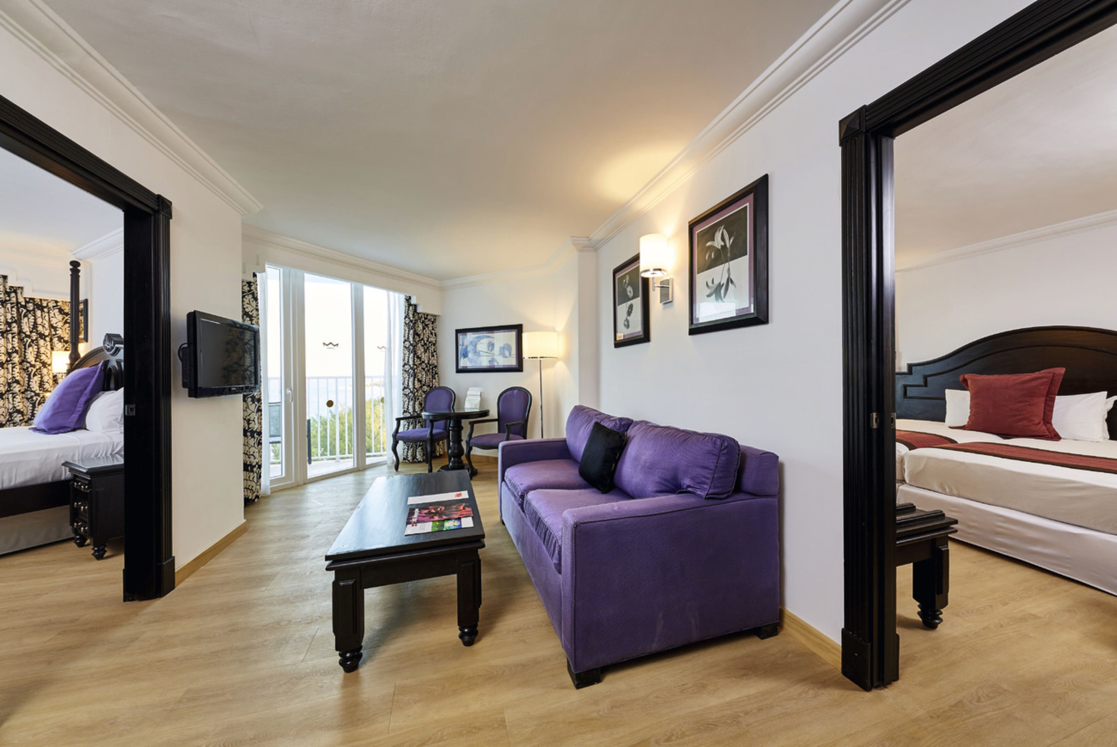 A modern hotel room with a bed, a purple sofa, a dining table, and a balcony with a view.
