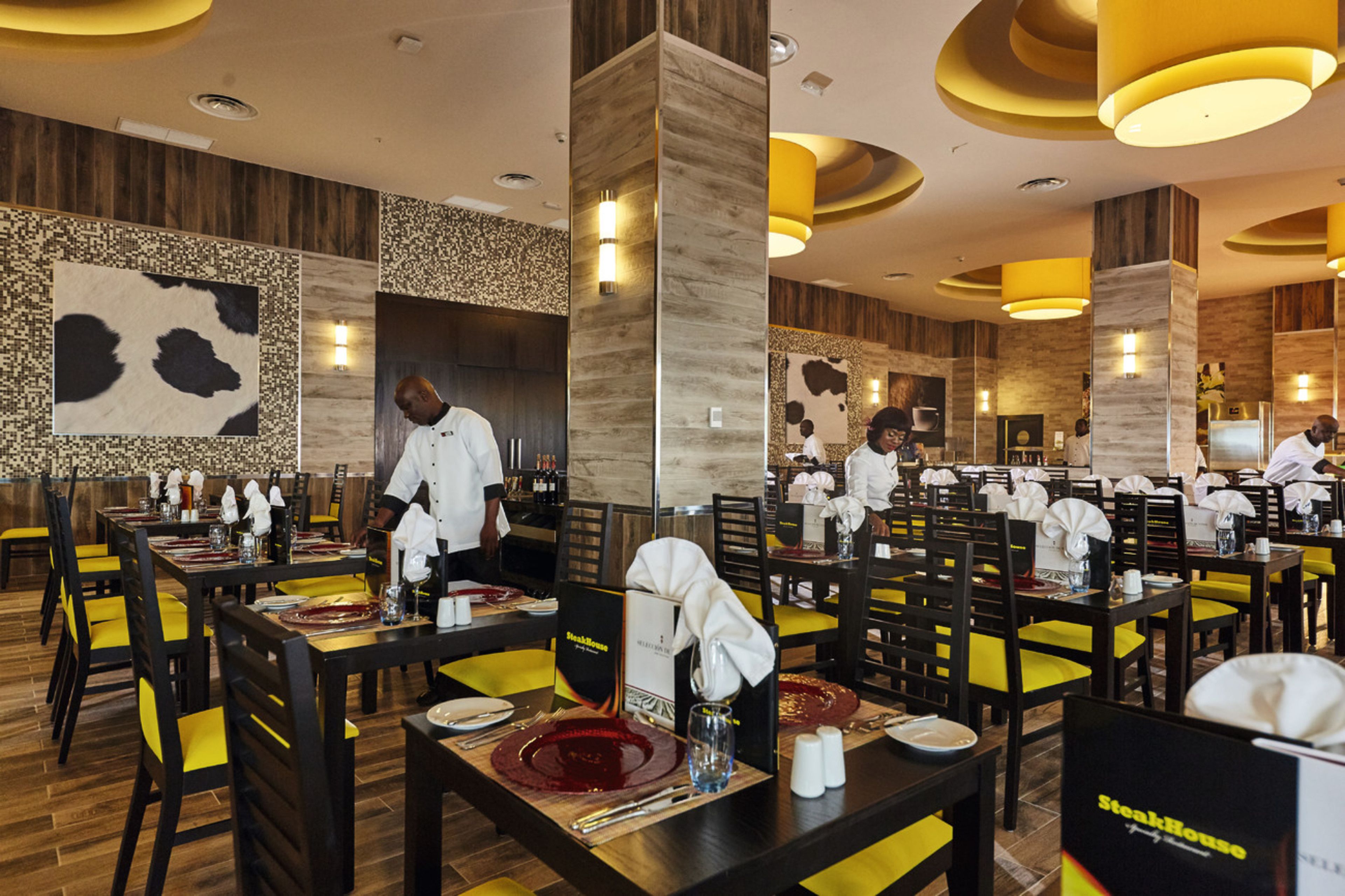 Restaurante com paredes de painel de madeira, cadeiras amarelas e mesas preparadas para refeições.