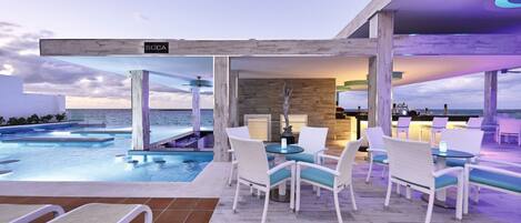 A rooftop pool area with lounge chairs and a bar, overlooking the ocean.