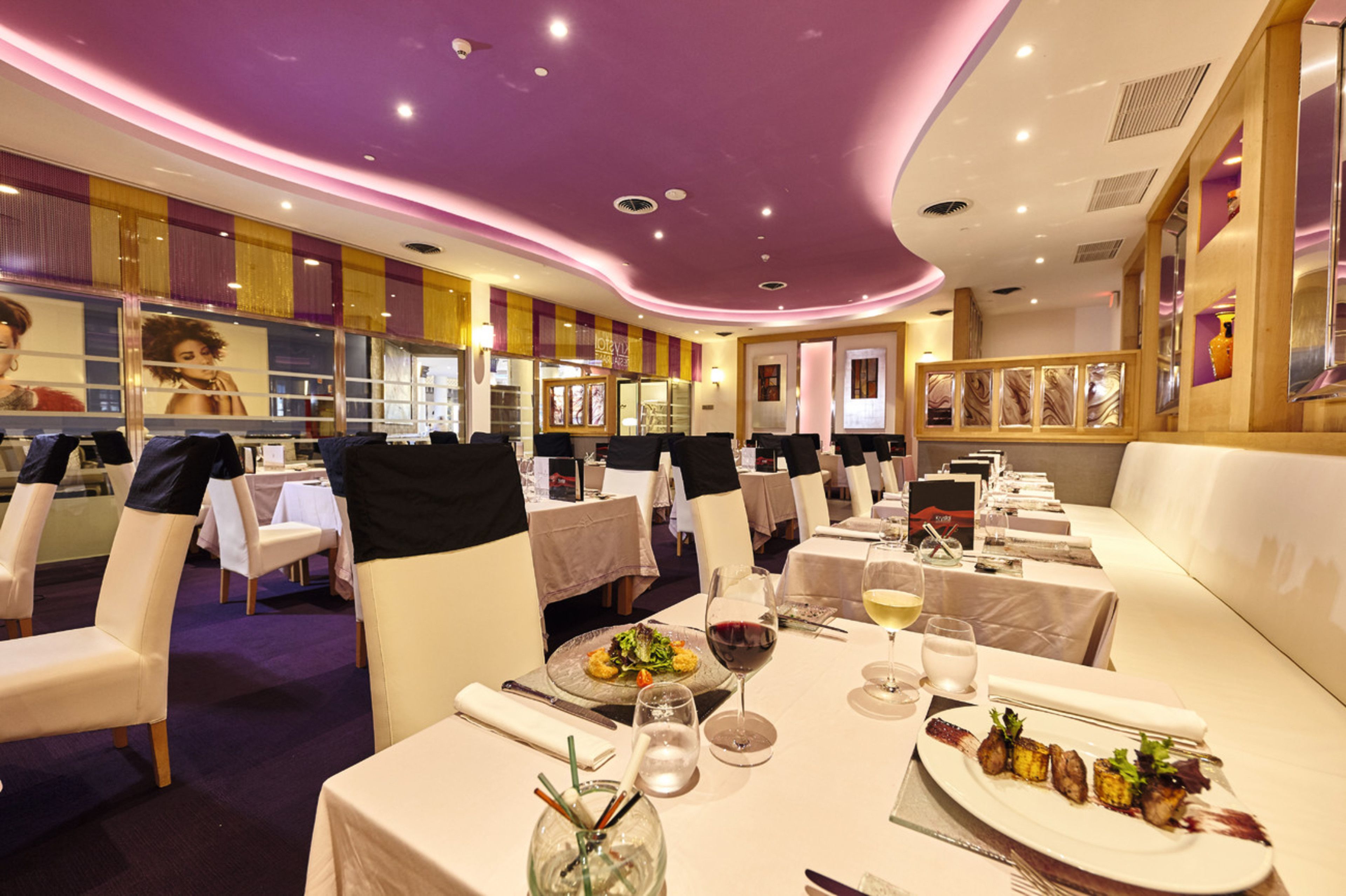 Un restaurant avec des tables et des chaises blanches, des touches de violet sur le plafond et un décor intérieur moderne.