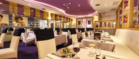 Un restaurant avec des tables et des chaises blanches, des touches de violet sur le plafond et un décor intérieur moderne.