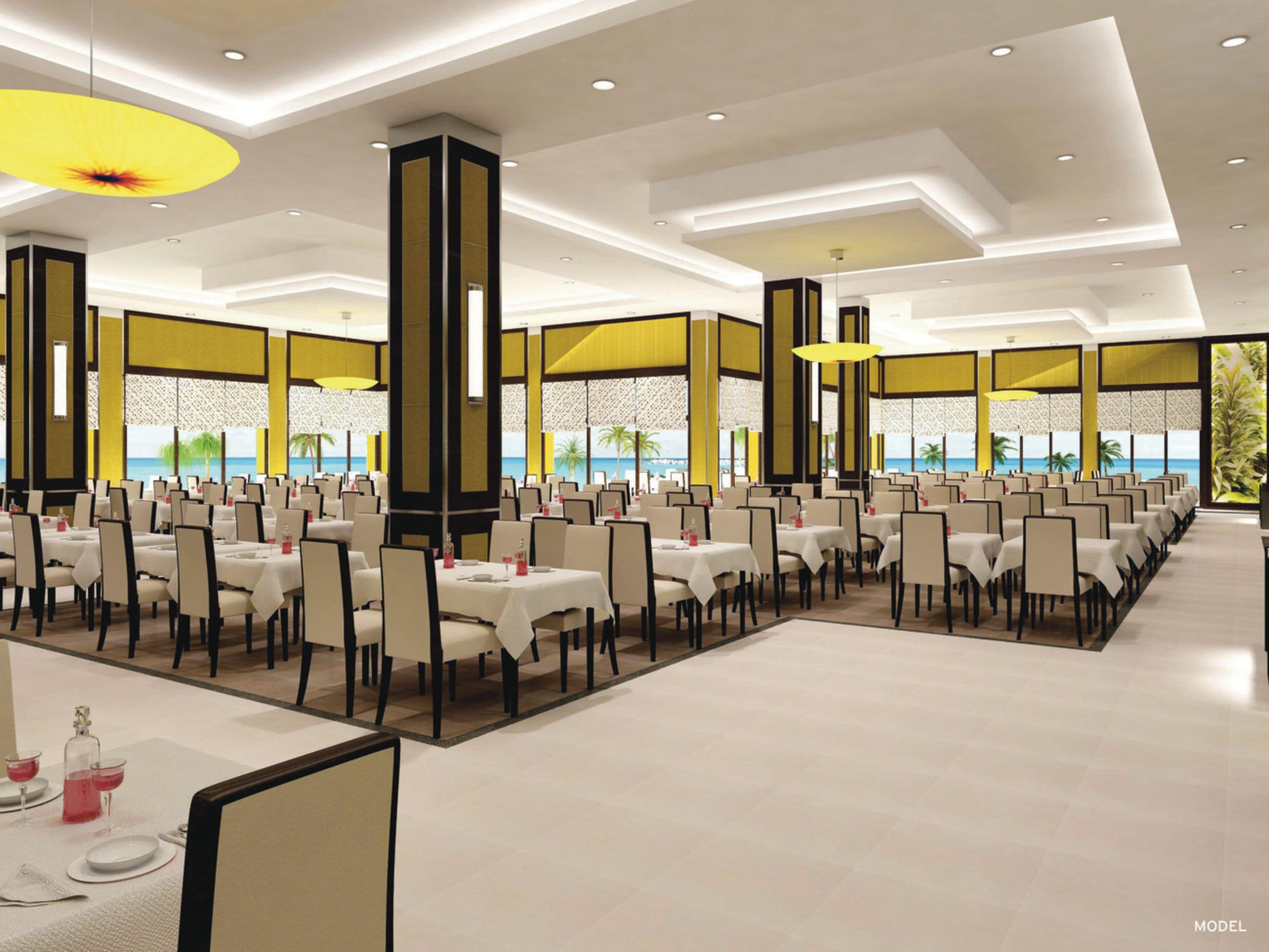 A spacious dining area with multiple tables and chairs, large windows offering a view of the sea, and modern ceiling design with recessed lighting.