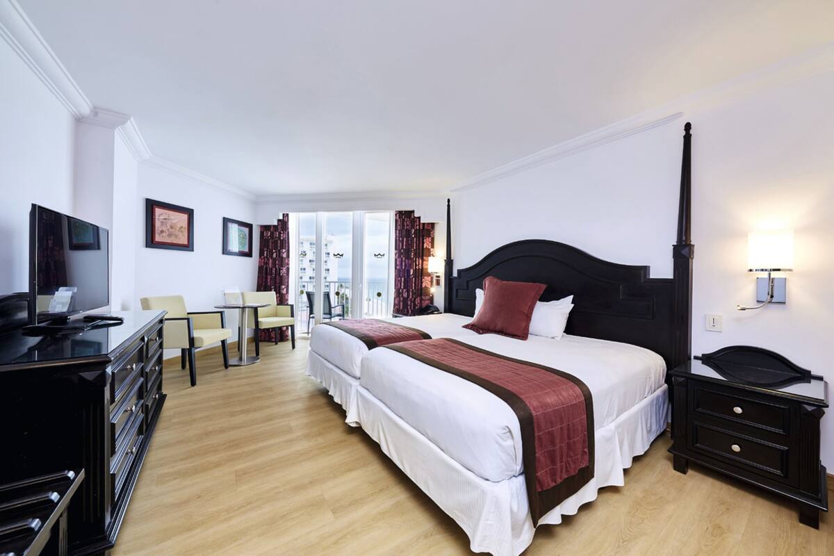 A hotel room with a large bed, a desk with a computer, a chair, and a TV.