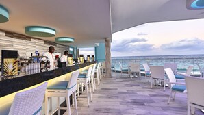 Eine Bar mit Meerblick, weißen Korbstühlen und einer Theke mit Barbereitungen.