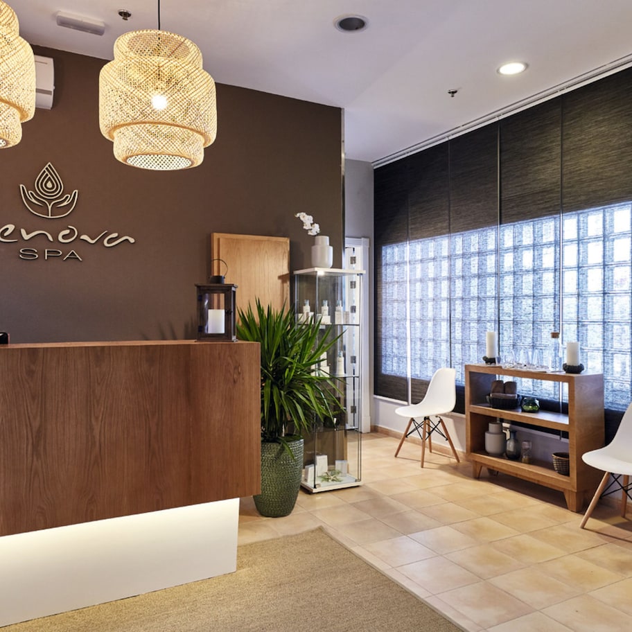A reception area with a wooden reception desk, two wicker pendant lights, a large window with a view, and a potted plant.