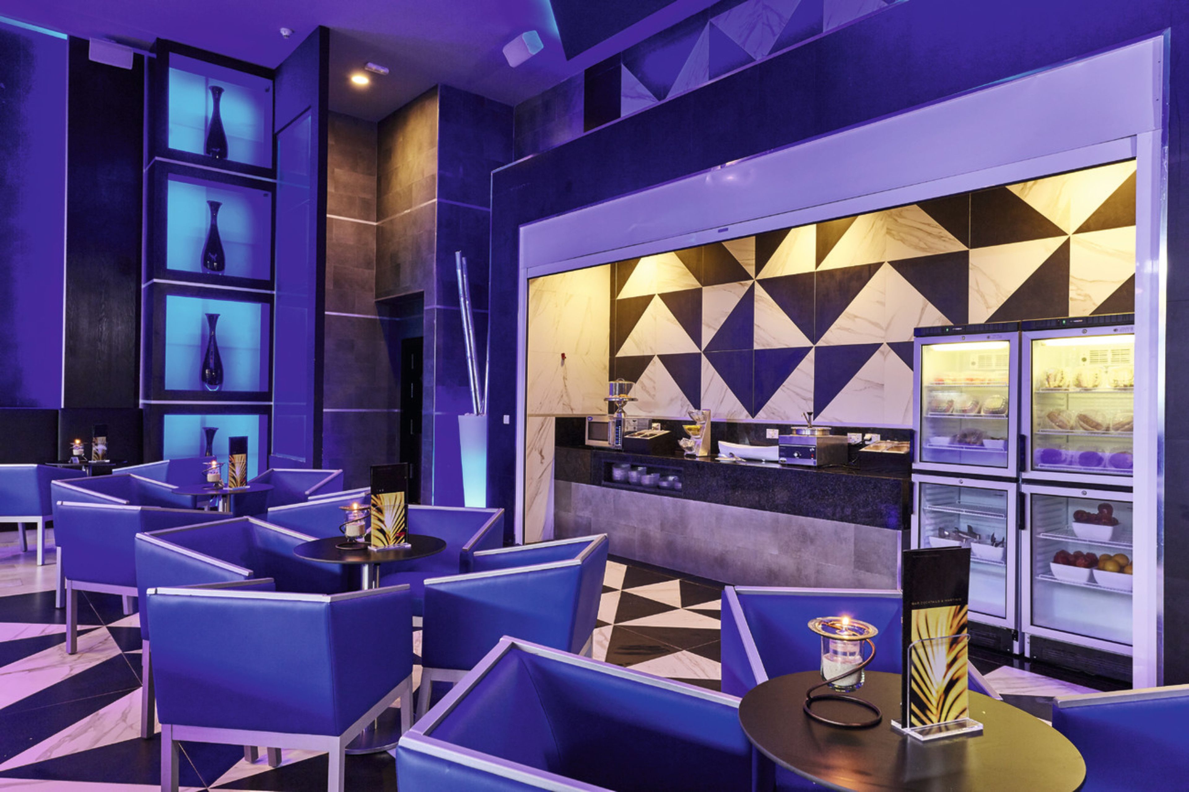 A modern hotel lobby with blue seating, a reception desk, and a geometric-patterned wall.