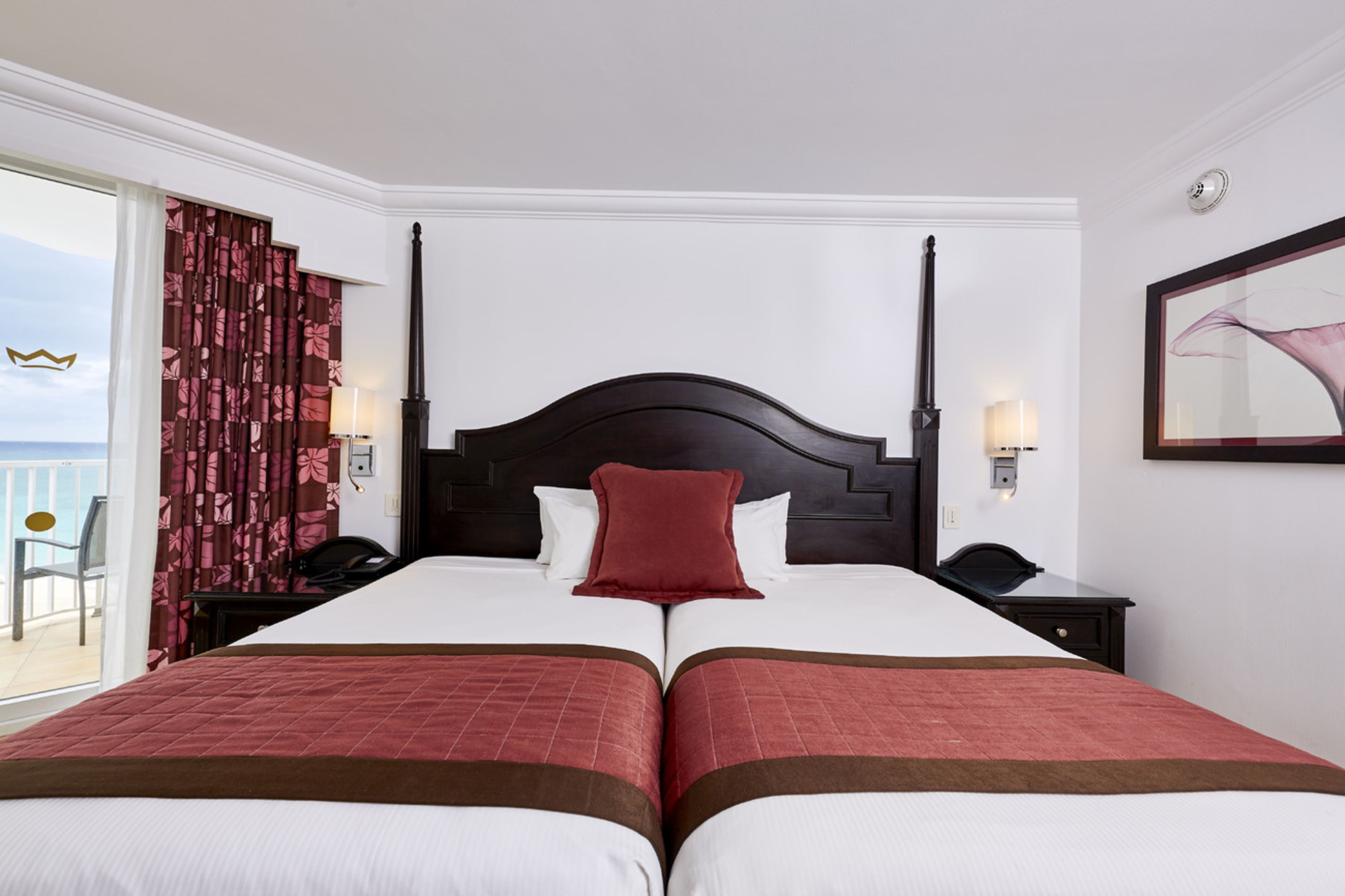 A double bed with a dark headboard, two bedside tables with lamps, and a view of the sea through a sliding door.