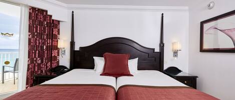 A double bed with a dark headboard, two bedside tables with lamps, and a view of the sea through a sliding door.