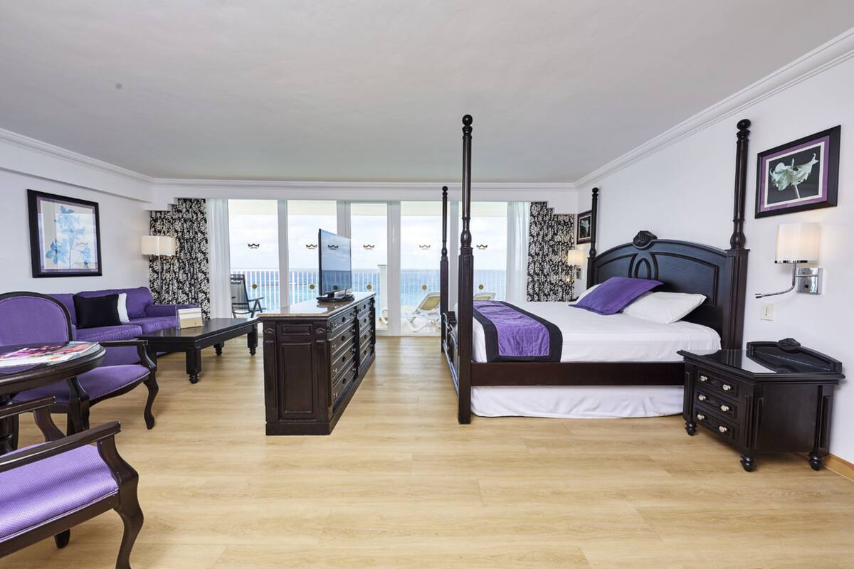 A four-poster bed with a view of the city, a purple sofa, a desk, and a dresser.