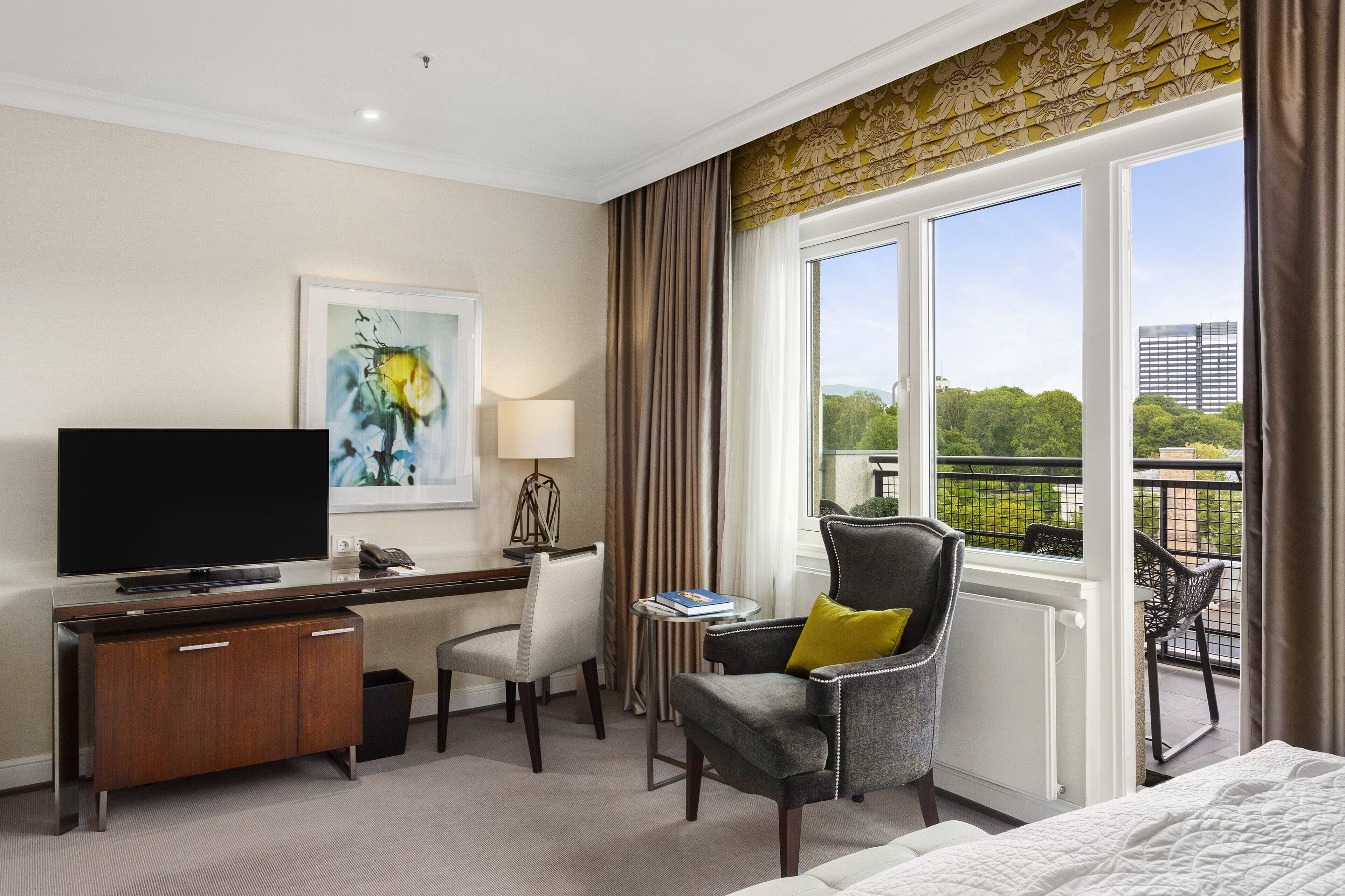 Een hotelkamer met een groot raam, een bureau met een flatscreen televisie, een comfortabele fauteuil en een bed.