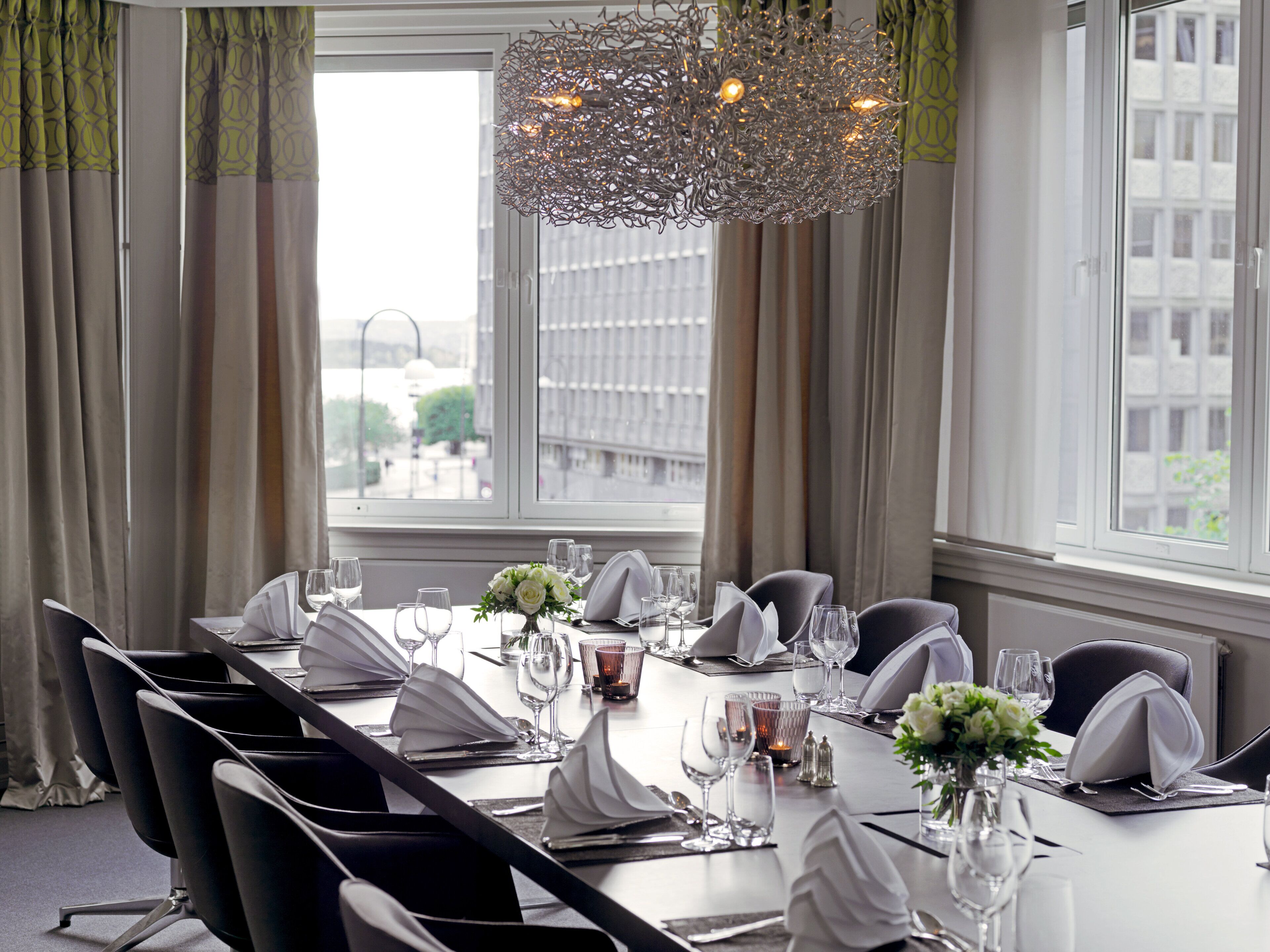 A conference room with a long table set for a meeting, large windows, and a decorative chandelier.