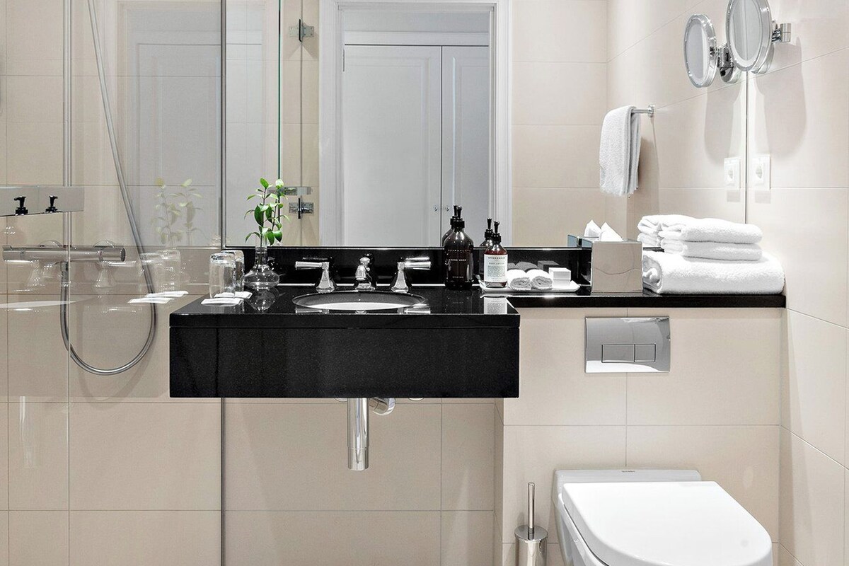 A modern bathroom with a glass-enclosed shower, a black countertop sink, a white toilet, and a mirror with two mirrors.