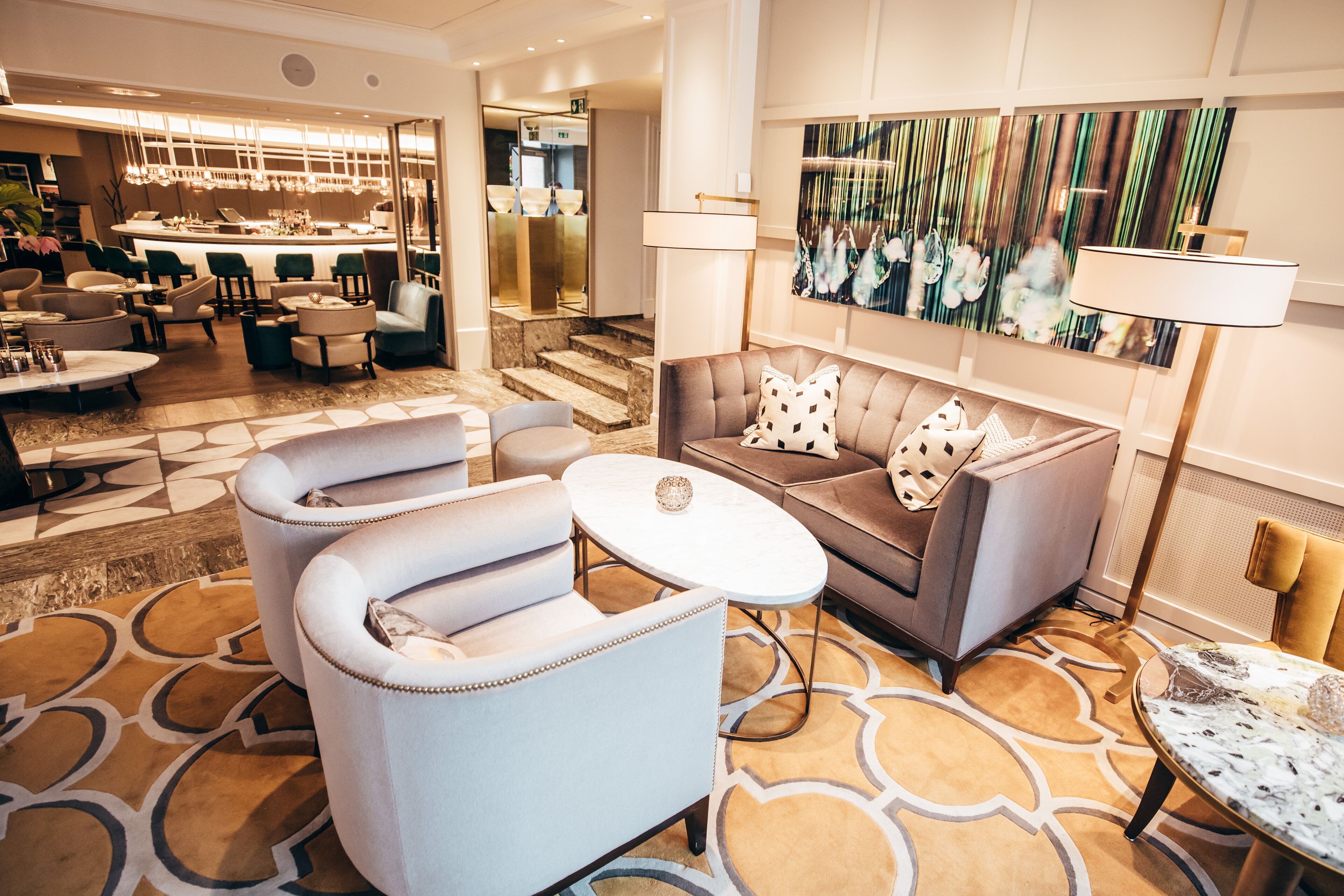 A modern lobby with a sofa, armchairs, a coffee table, and a bar area.