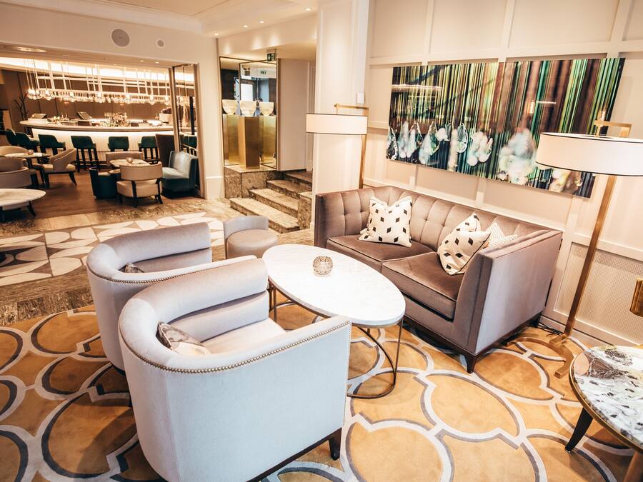 A modern lobby with a sofa, armchairs, a coffee table, and a bar area.
