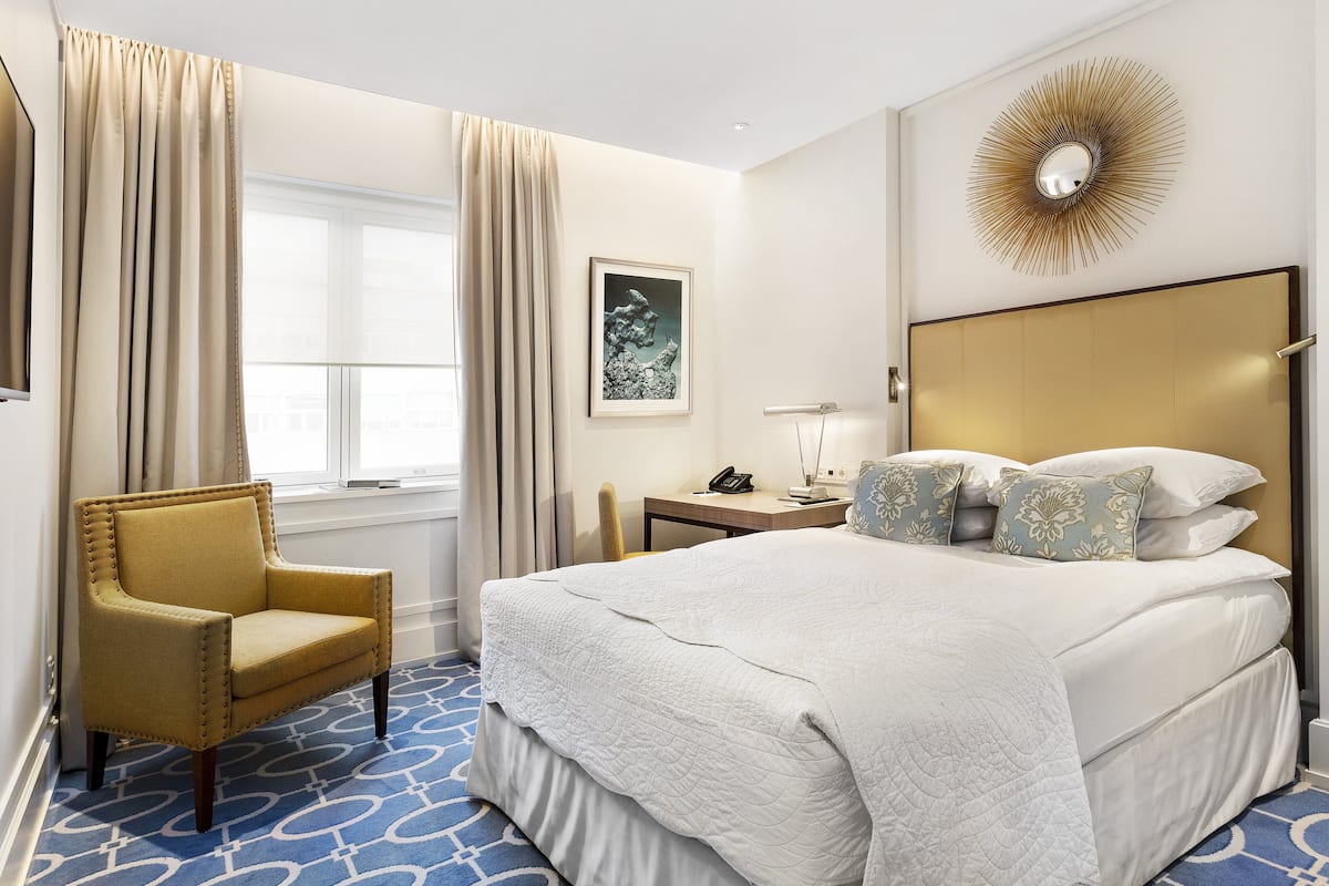 A hotel room with a large bed, a chair, a desk, and a window with curtains.