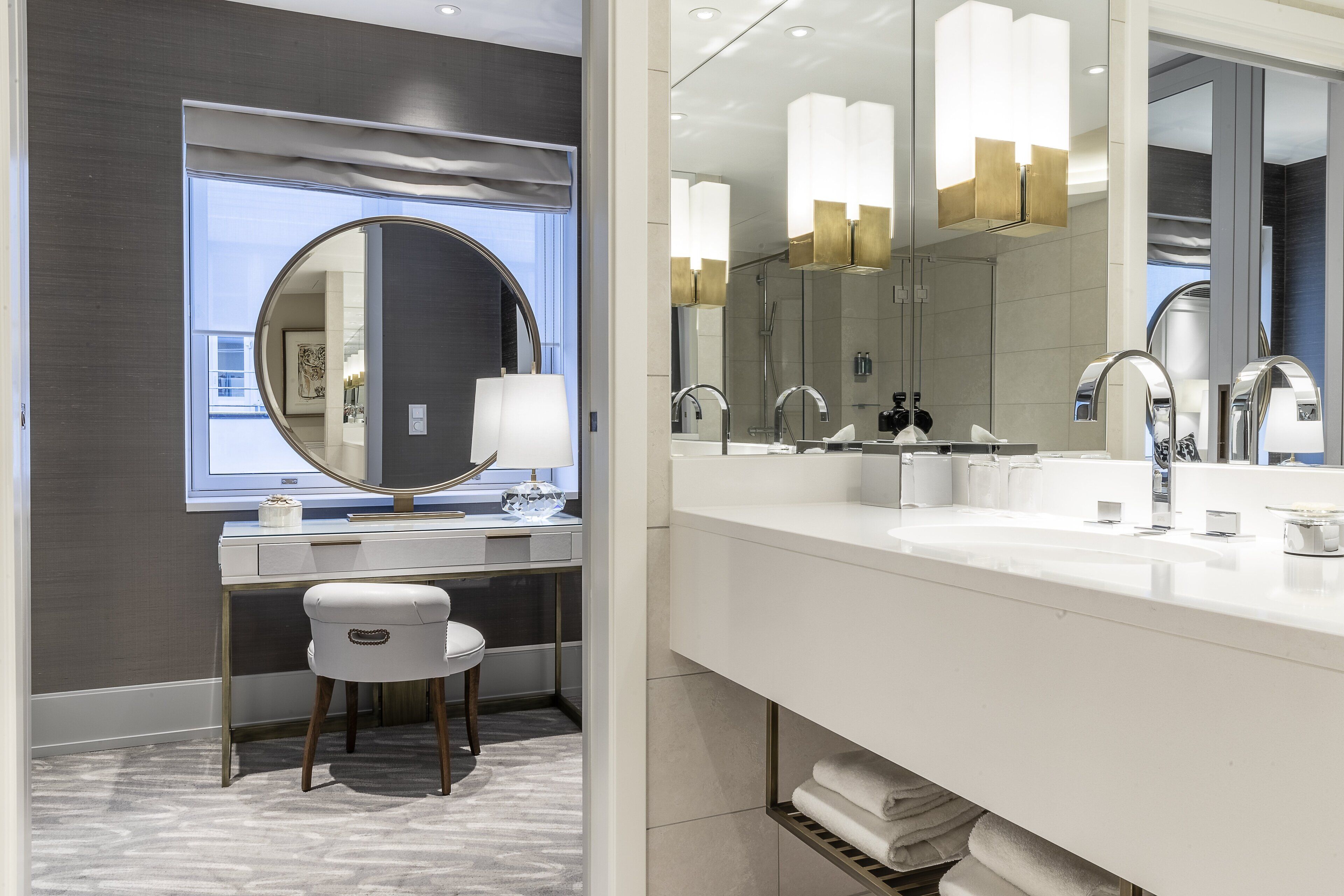 Un baño moderno con un espejo grande, lavamanos dobles y un mueble de tocador con un taburete.