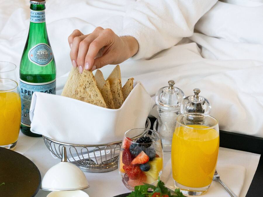 A breakfast tray with toast, avocado, berries, and orange juice on a bed.