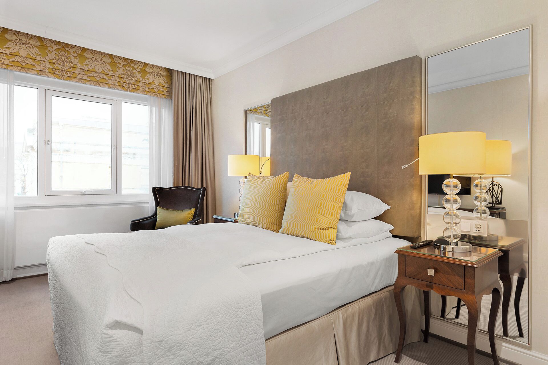 Habitación de hotel con una cama grande, dos lámparas de noche, una mesita de noche y un espejo.