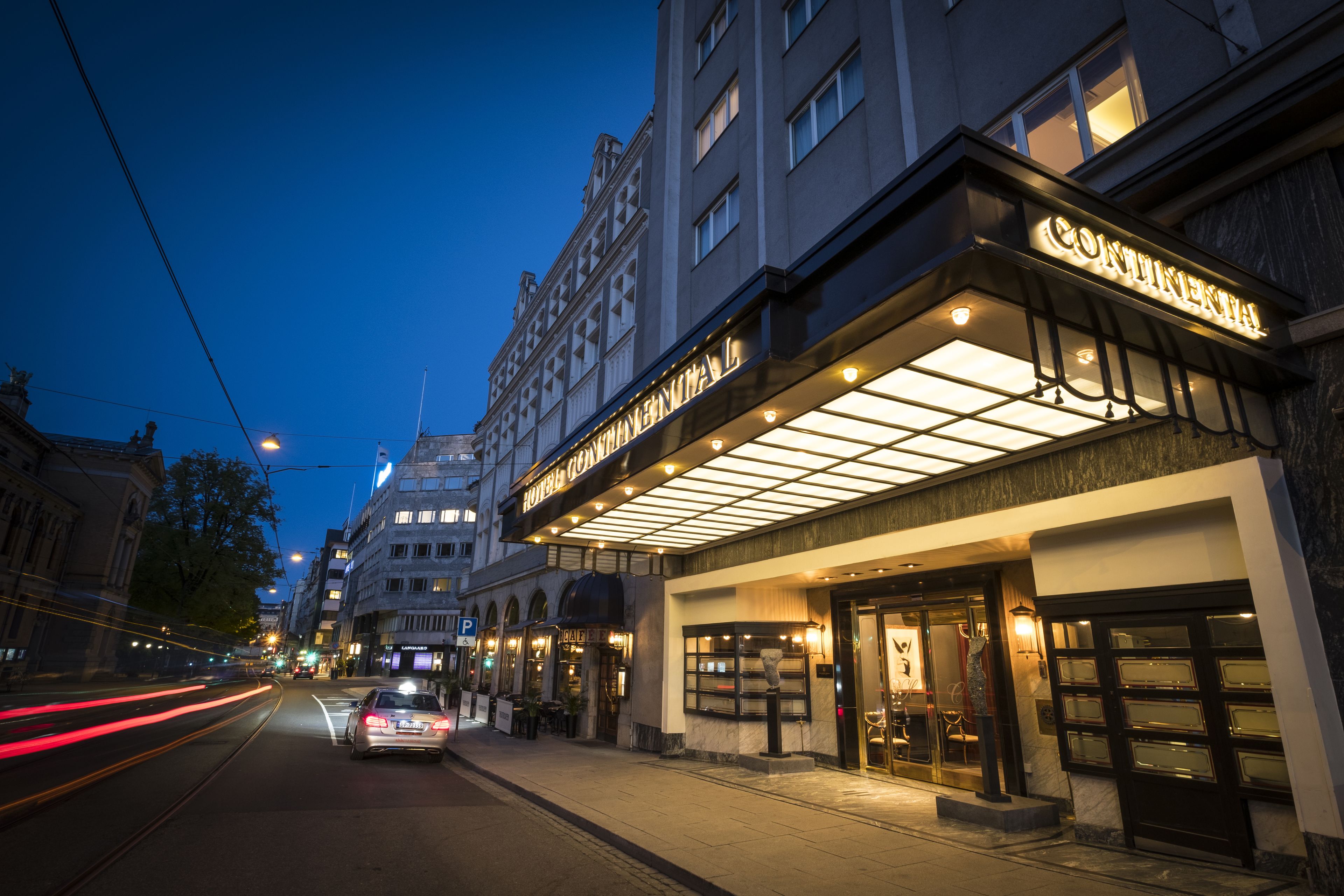 A hotel with a marquee sign, a well-lit entrance, and a street view with moving vehicles.