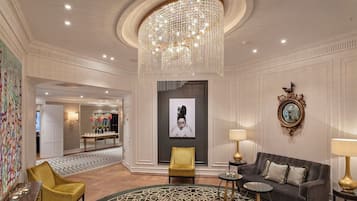 Eine luxuriöse Lobby mit einem prunkvollen Chandelier, einem Essbereich mit einem gemusterten Teppich und einem modernen Sofa mit Spiegel und Lampe.