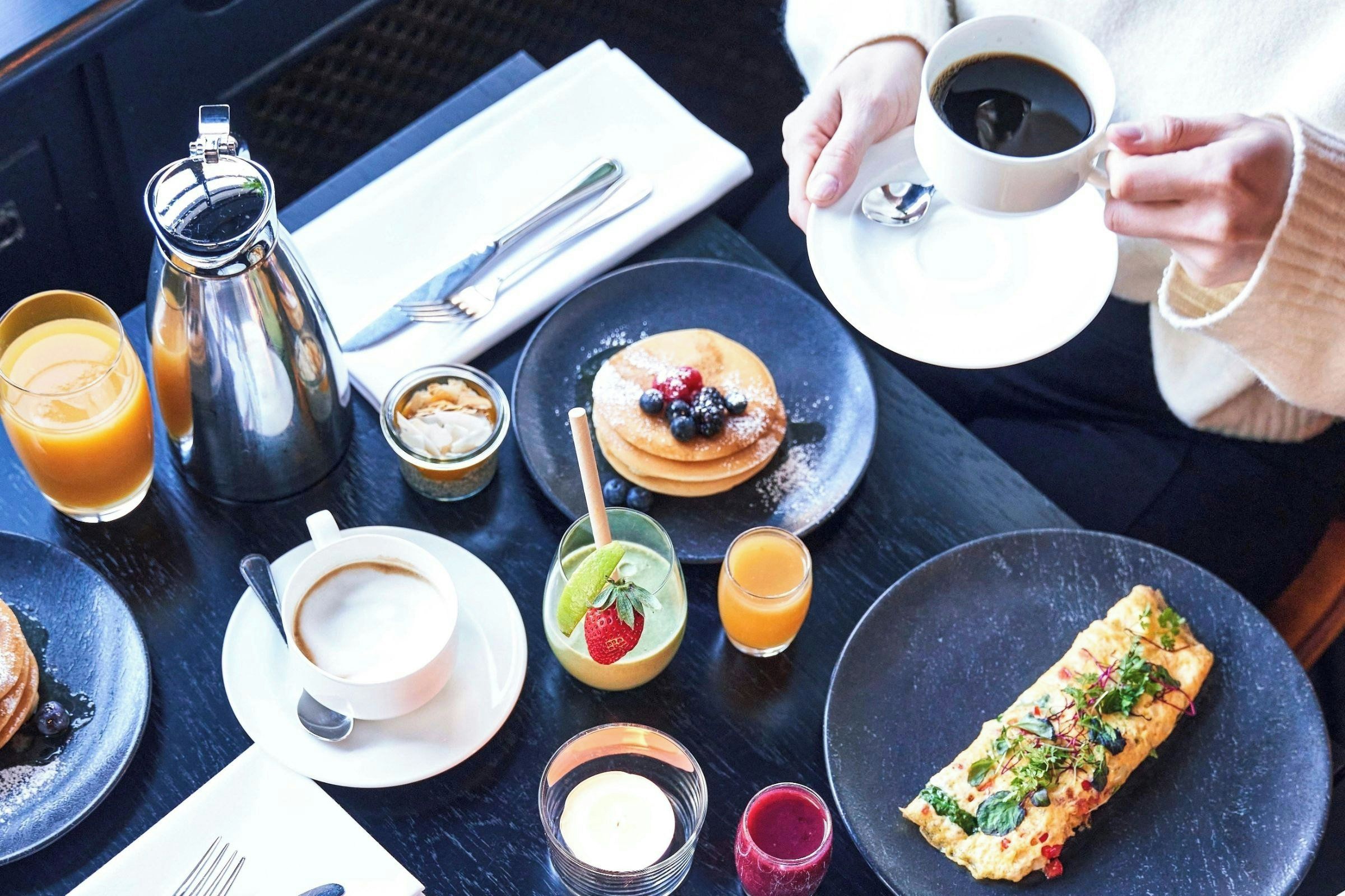 A breakfast setting with pancakes, coffee, juice, and a rolled omelette on a table.