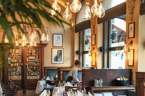 A restaurant interior with hanging light bulbs, framed artwork on the walls, and a person seated at a table. - Hotel Continental (Oslo)