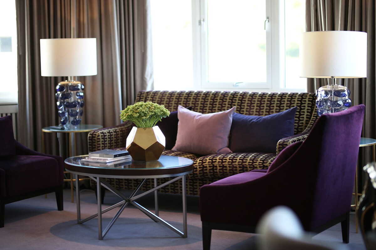 A living room with a patterned sofa, a round coffee table with a plant, and two lamps.