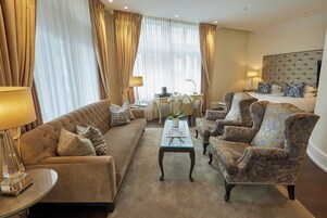 Una habitación de hotel elegante con sofá, sillones, una mesita de centro y una cama con cabecero capitonado.