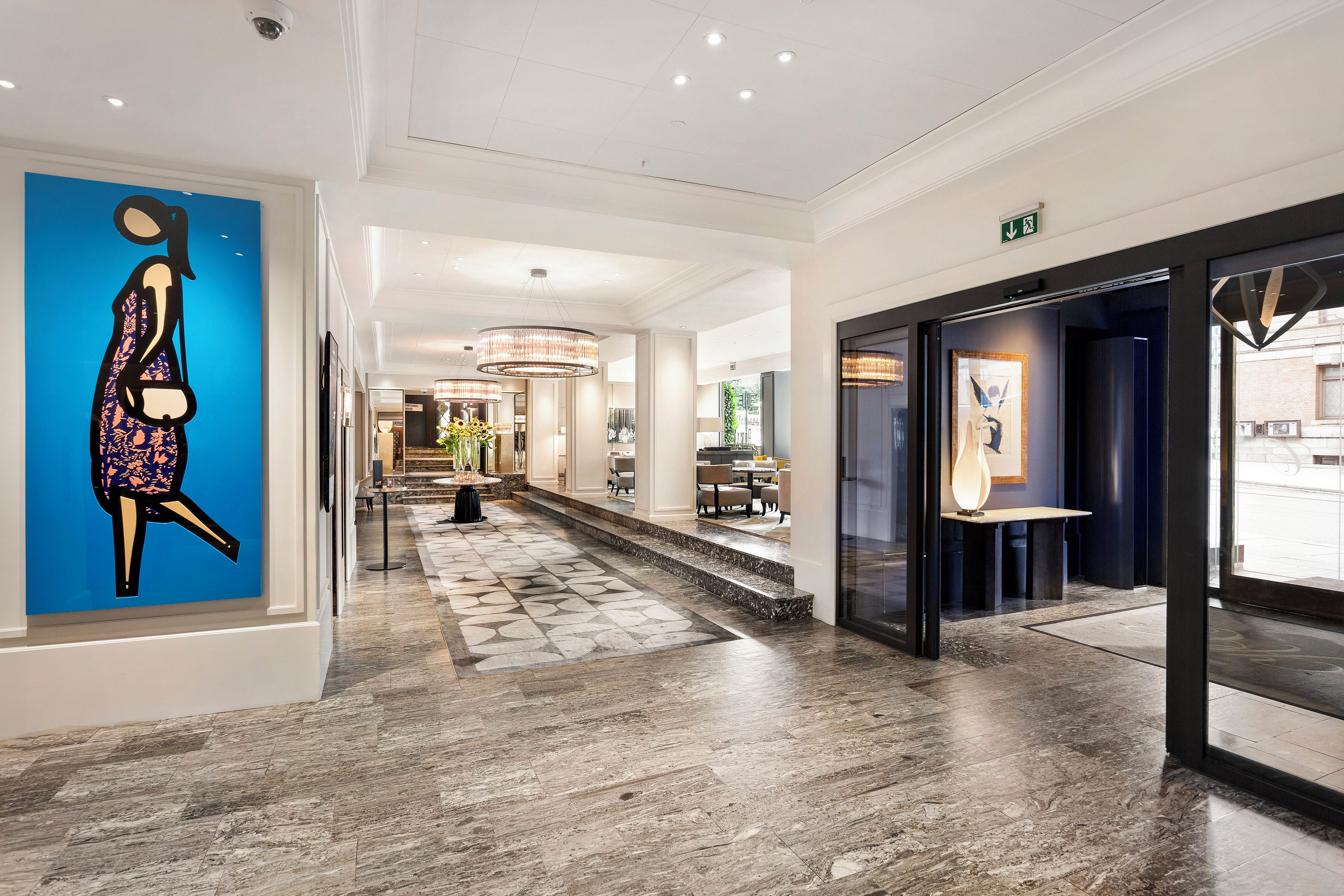 Ein Hotelkorridor mit einem blauen Wandbild, einer Treppe und einer Glastür zu einem Restaurant.