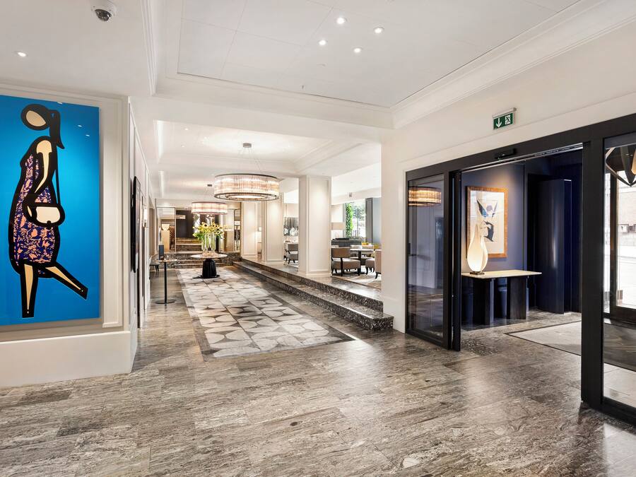 Ein Hotelkorridor mit einem blauen Wandbild, einer Treppe und einer Glastür zu einem Restaurant.