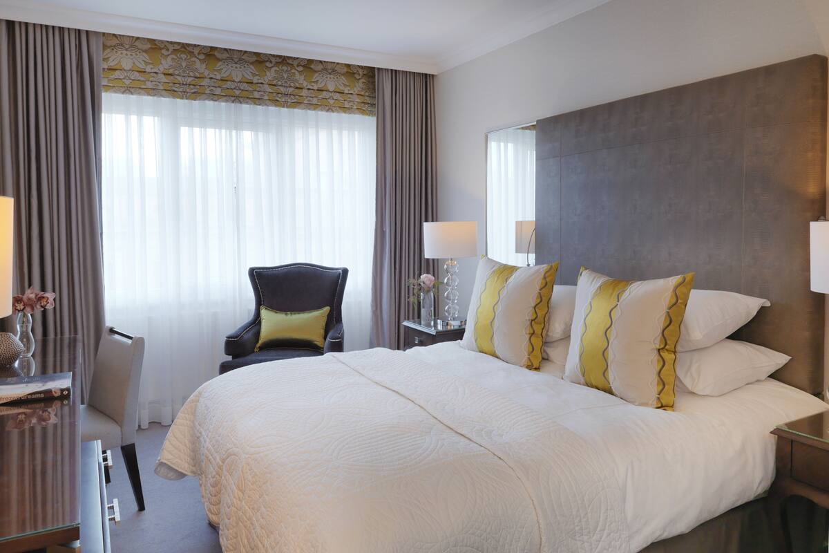 A hotel room with a large bed, a desk, a chair, and a nightstand with lamps.