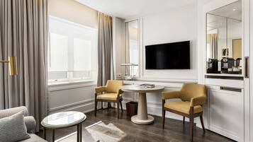 A hotel room with a sofa, two armchairs, a small table, a TV, and a minibar.