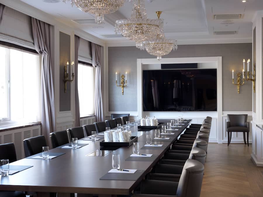 A conference room with a long table, chairs, and a large screen.