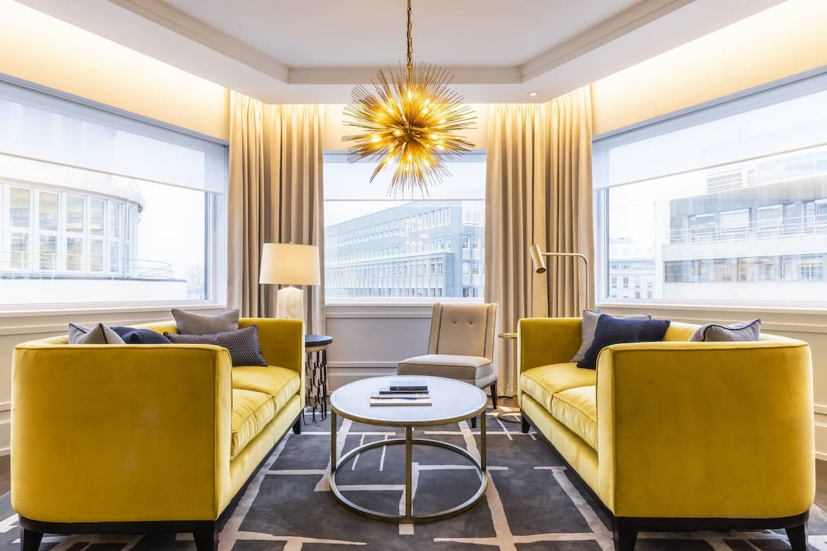 A modern hotel room with yellow sofas, a round coffee table, and a unique starburst chandelier.