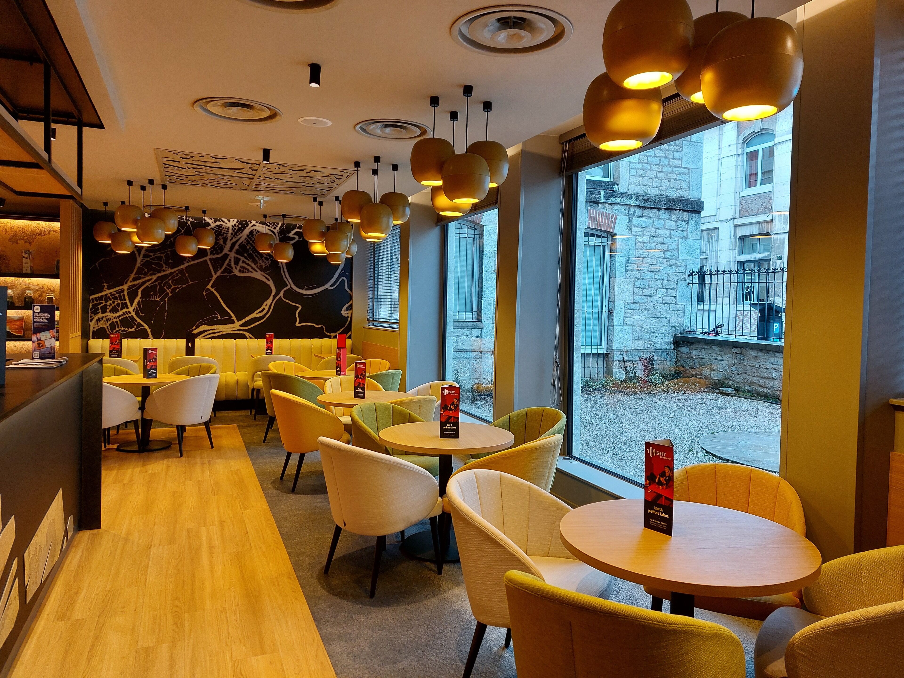 A modern restaurant interior with yellow and white chairs, round tables, and pendant lighting.