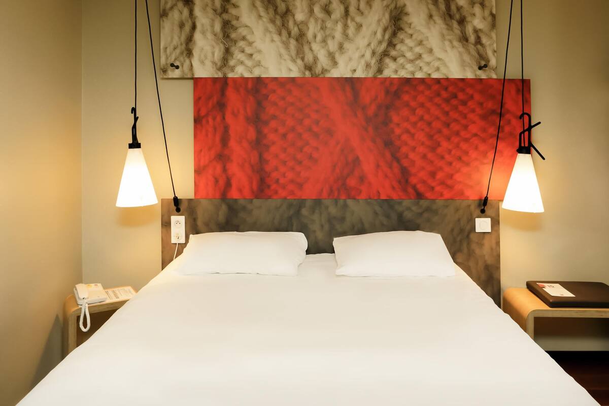 A hotel room with a large bed, two bedside tables, a telephone, and a wall-mounted lamp.