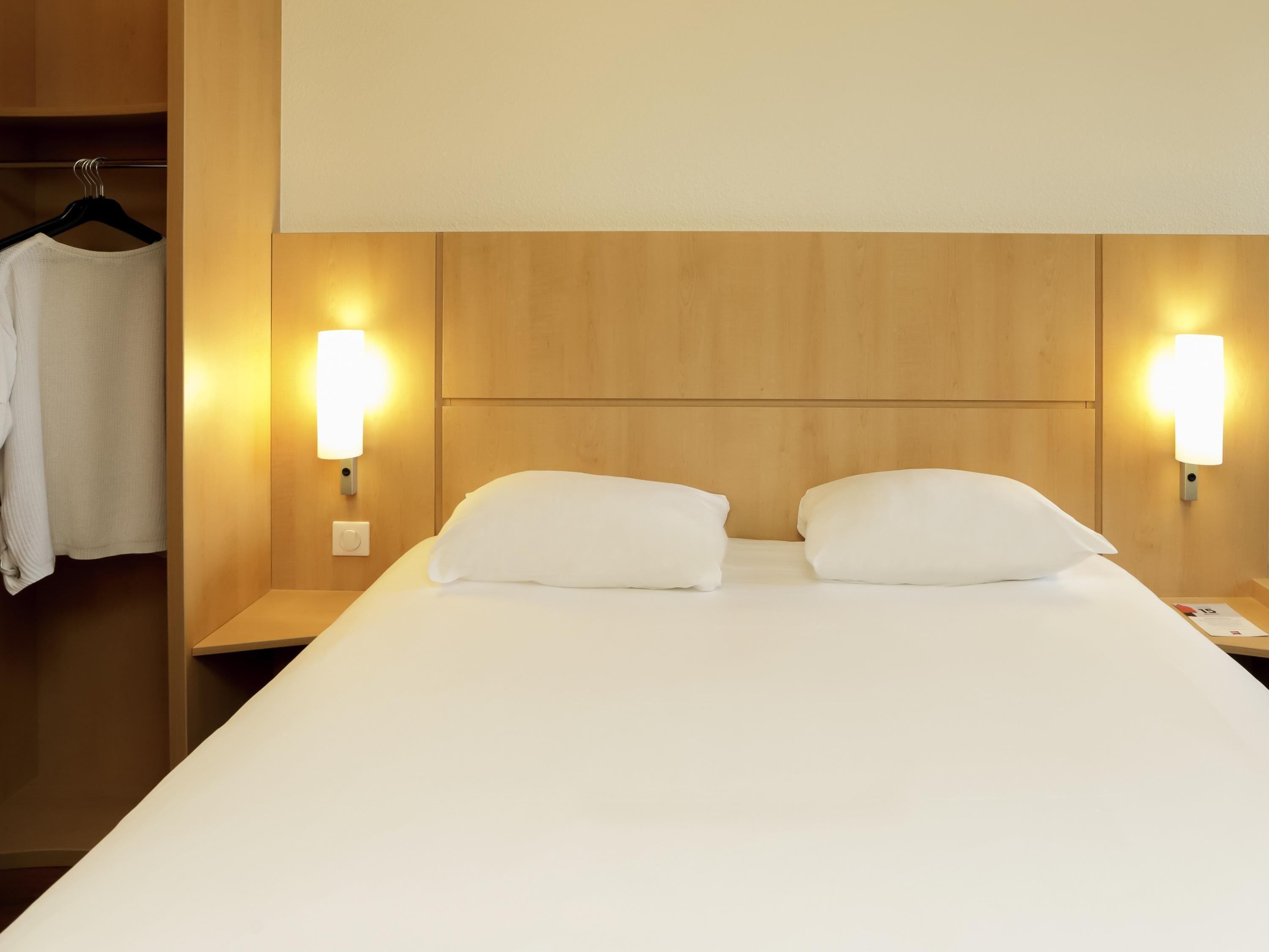 Une chambre d’hôtel avec un lit, deux lampes de chevet, une table de chevet et une robe suspendue.
