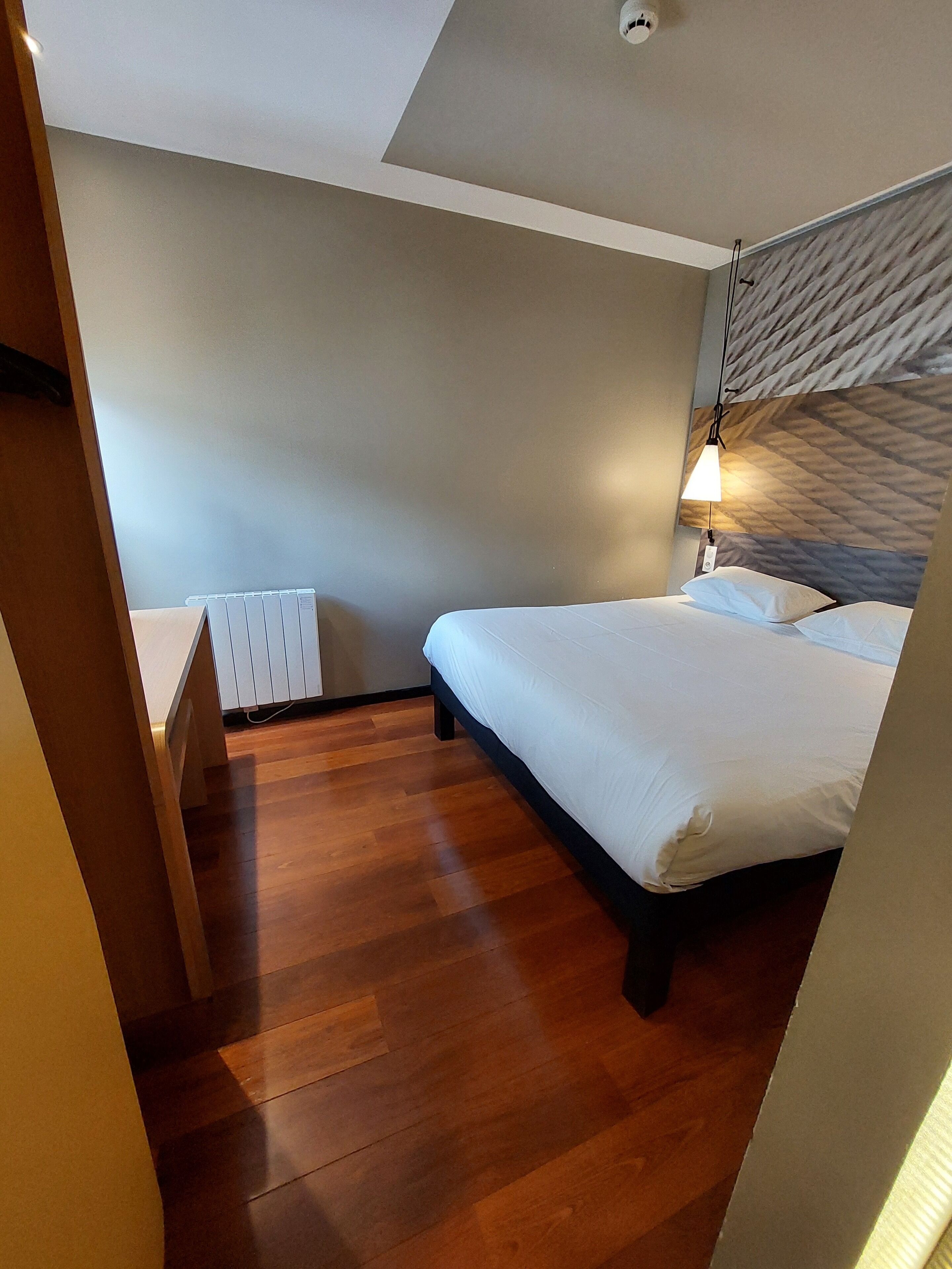 A bedroom with a wooden floor, a bed with white bedding, a radiator, and a textured wall.