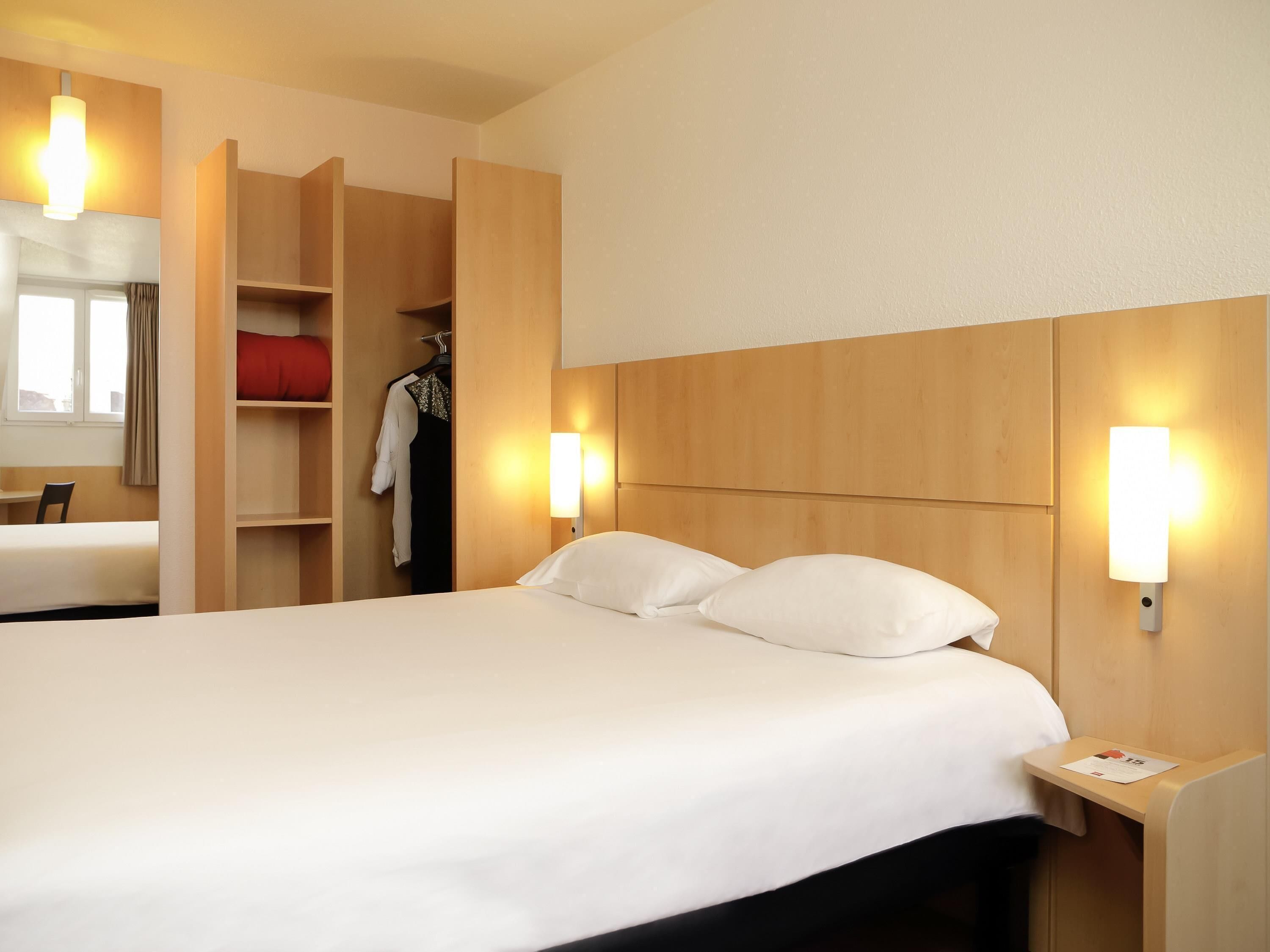 A hotel room with a bed, bedside tables, a wardrobe, and a mirror.