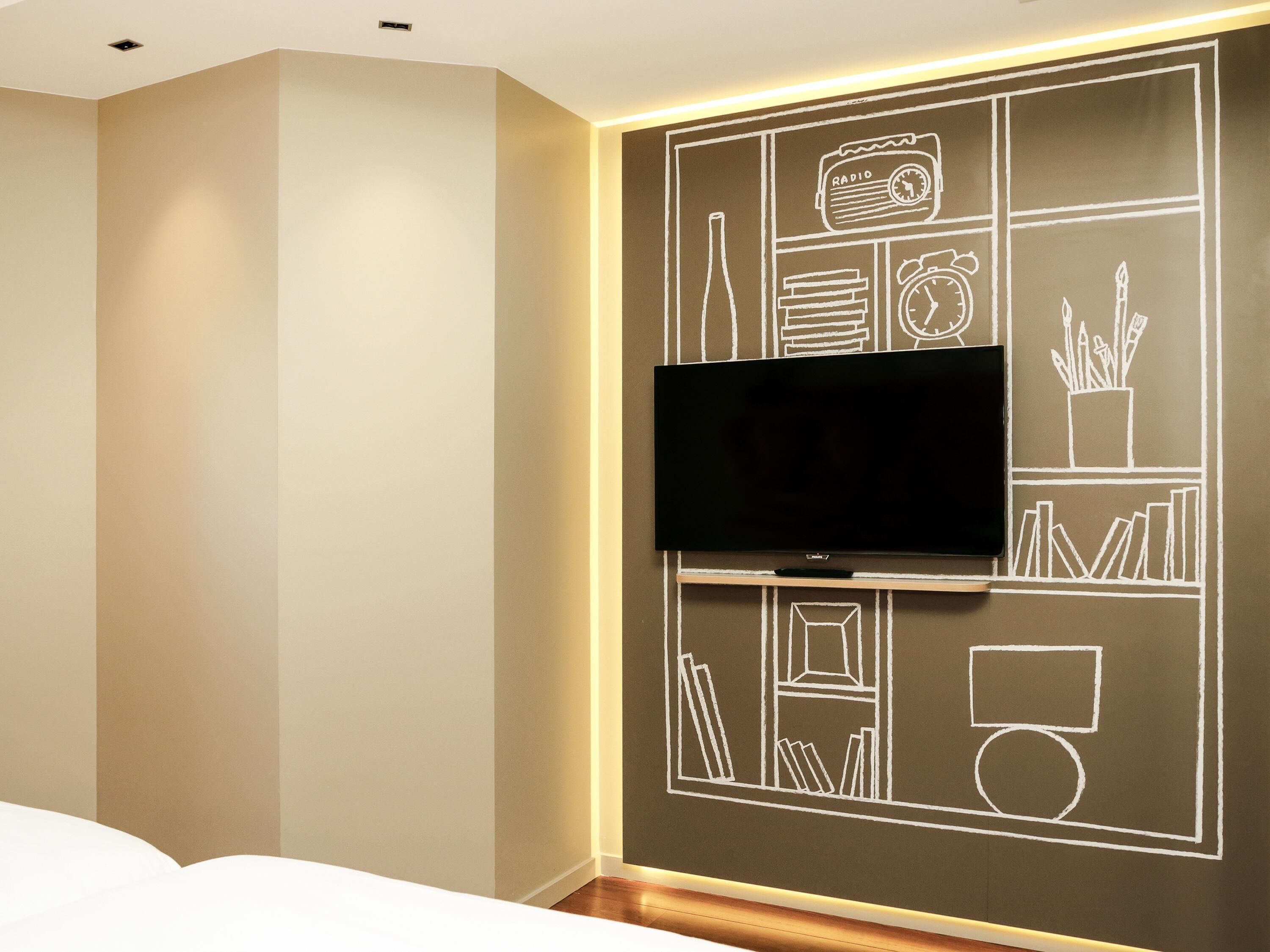 A modern hotel room with a flat-screen TV mounted on a wall with a chalkboard design.