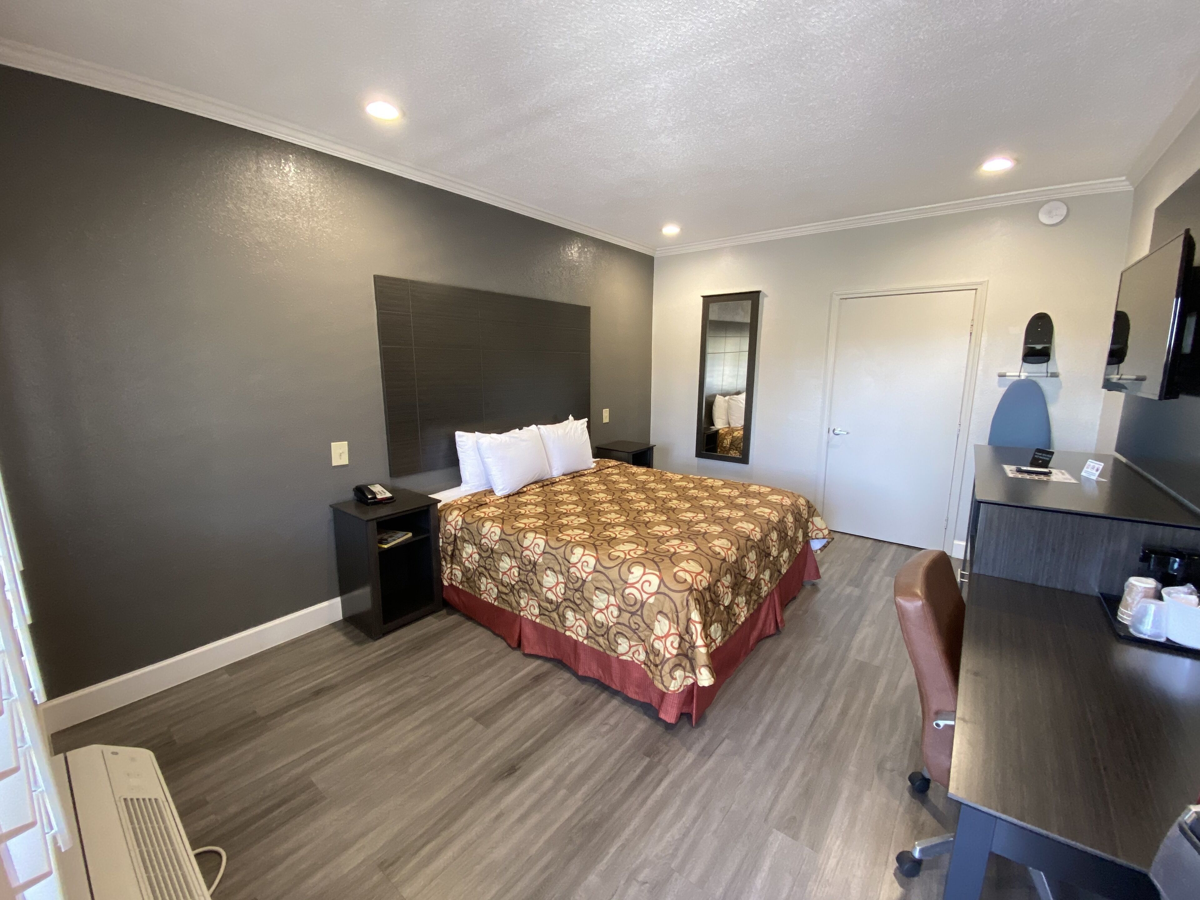 Ein Hotelzimmer mit einem großen Bett, einem Schreibtisch, einem Sessel, einem Spiegel und einem Kleiderschrank.