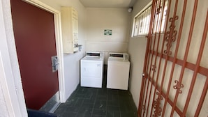 A laundry room with two washing machines, a sign indicating guest laundry hours, and a security camera.